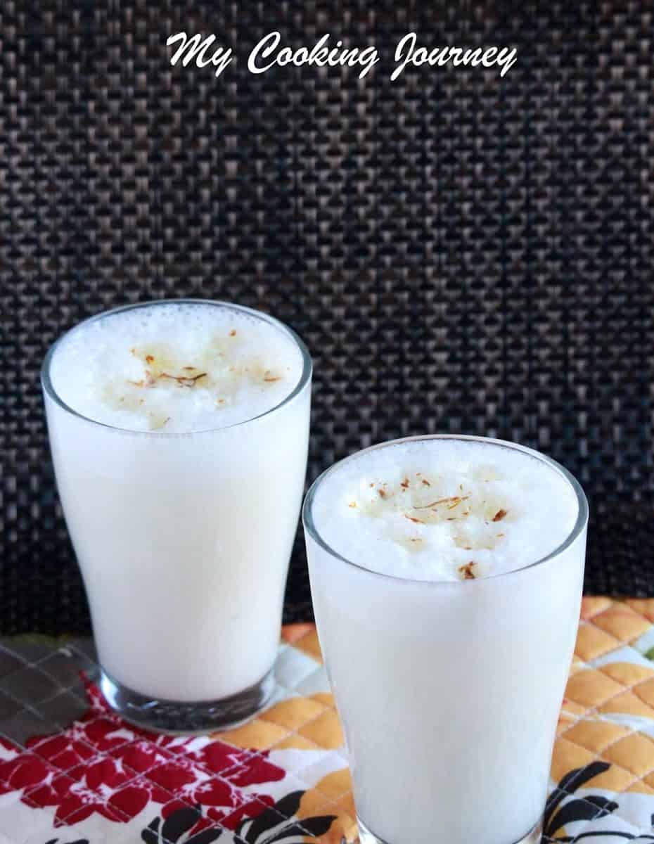 Lassi Patiala with saffron on top in two tall glasses. 
