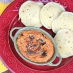 orange color chutney with seasonings on top and idli on side