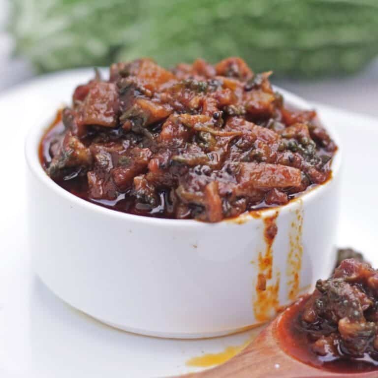Bitter gourd pickle in a white bowl with oil dripping on the side