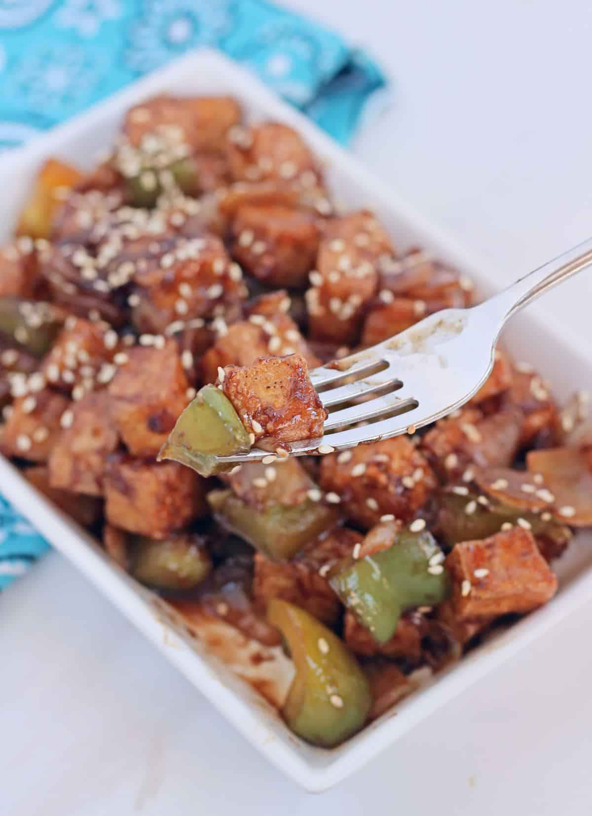 A single tofu and bell pepper in a fork and more in the plate