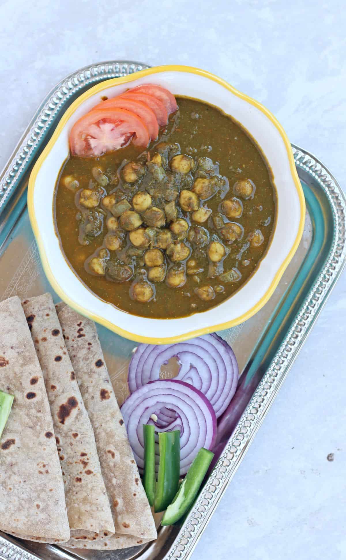 chana in palak subzi with roti and sliced onion and green chilies on side.