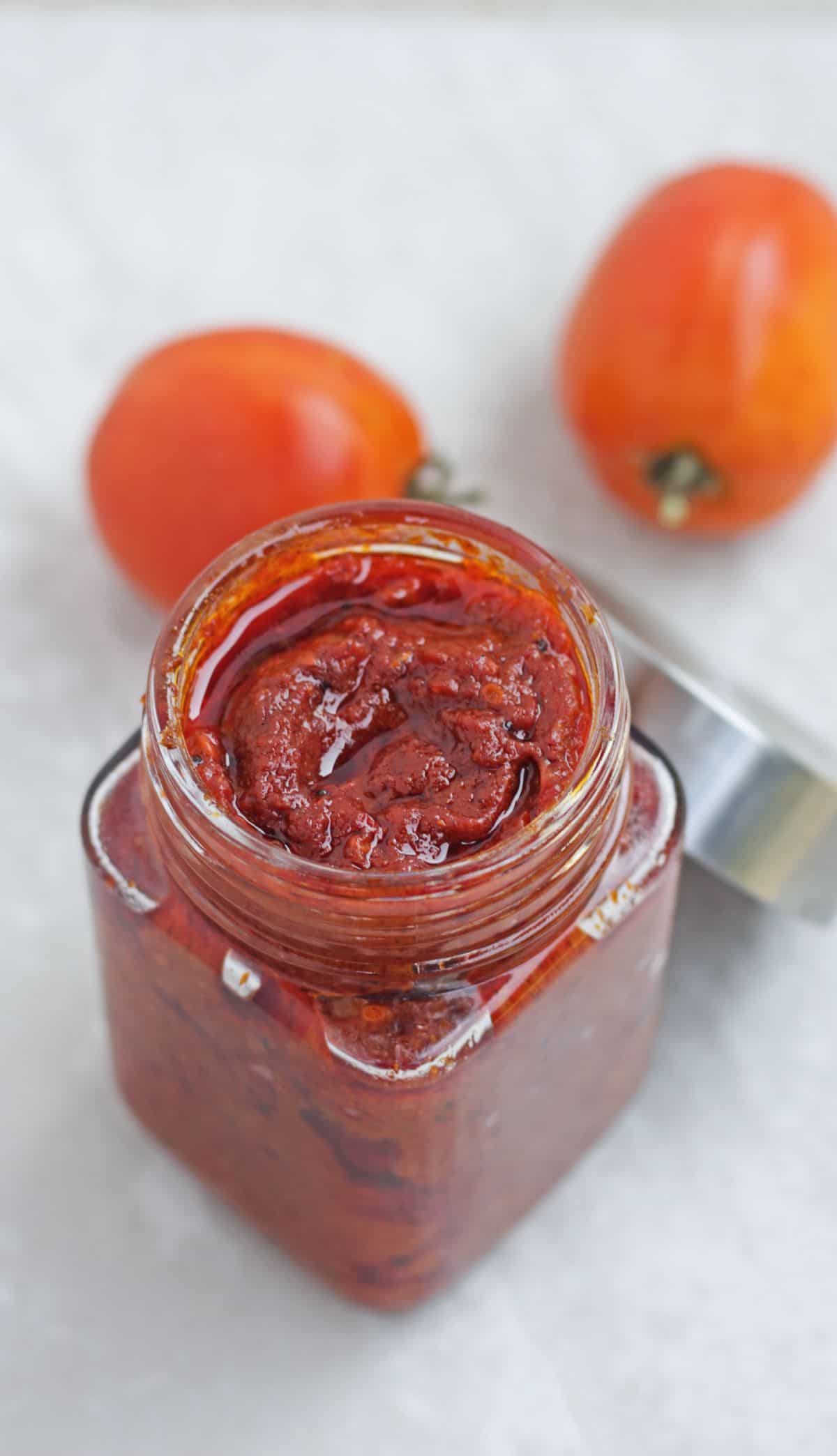 tomato pickle in a jar with tomatoes in the background