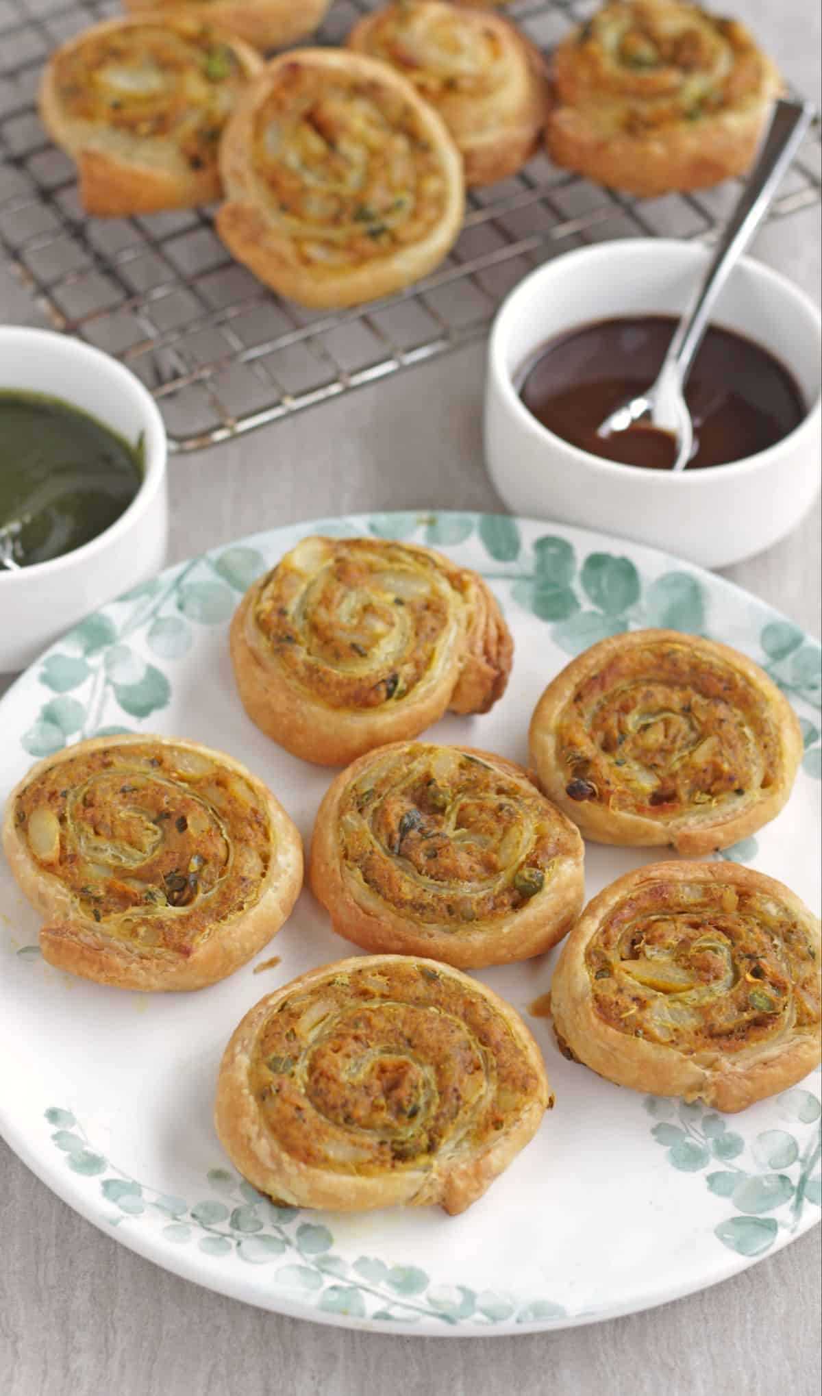 puff pastry pinwheel samosa in a white plate with red and green chutney on the side