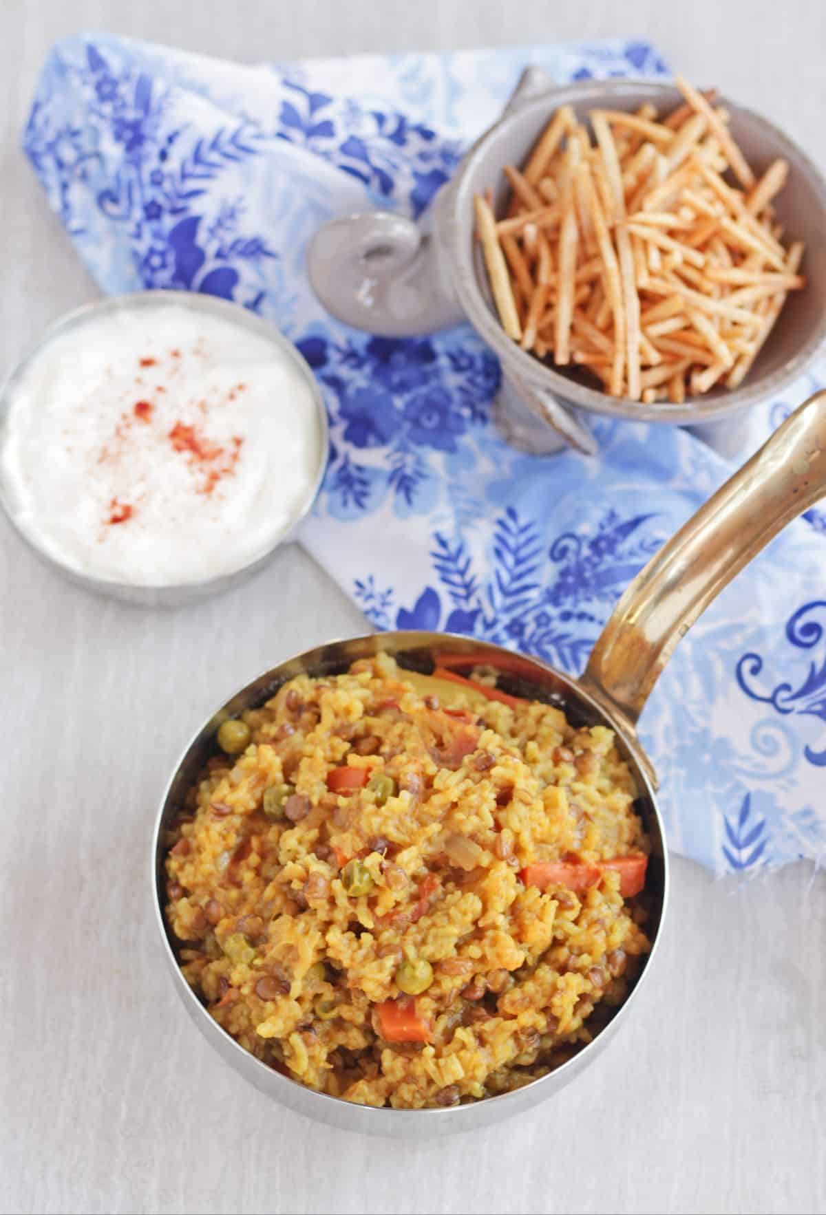 vegetable masala khichdi with yogurt and chips in the background