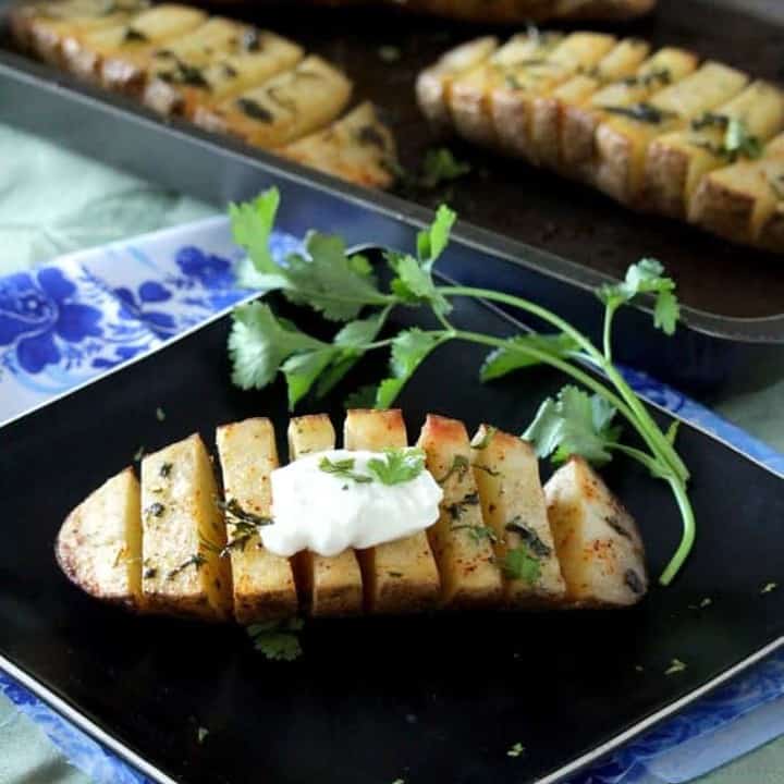 Scored Potatoes in a black plate with sour cream on top - Featured Image