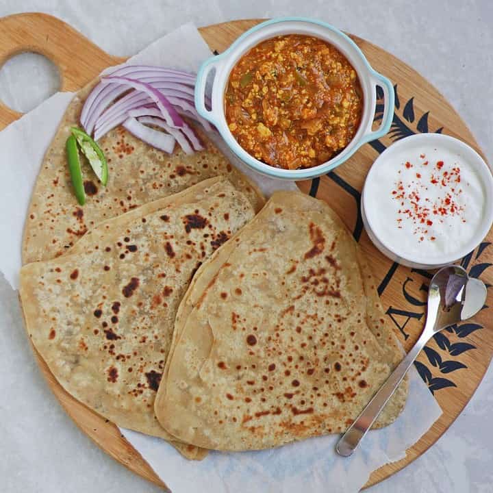a lunch platter with paratha, subzi and yogurt along with salad.