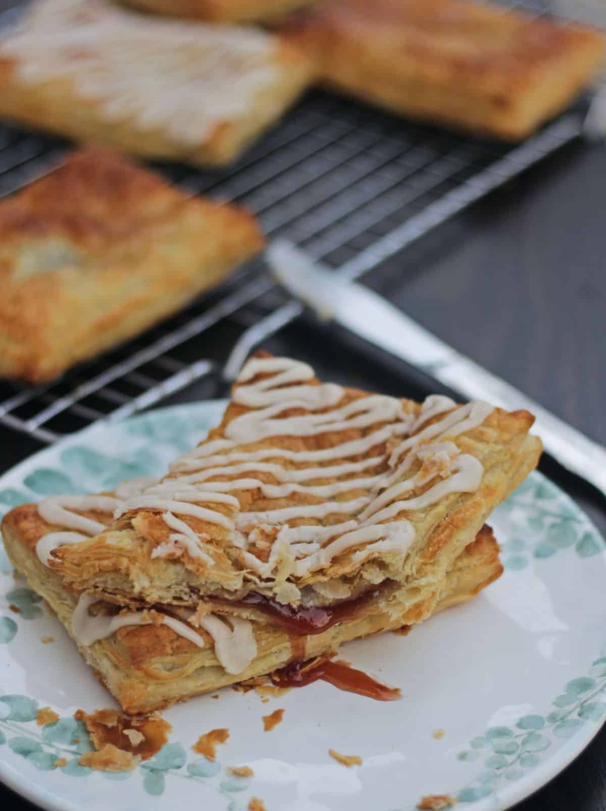 Two toaster strudel in a plate with one bit a little and jam oozing out.